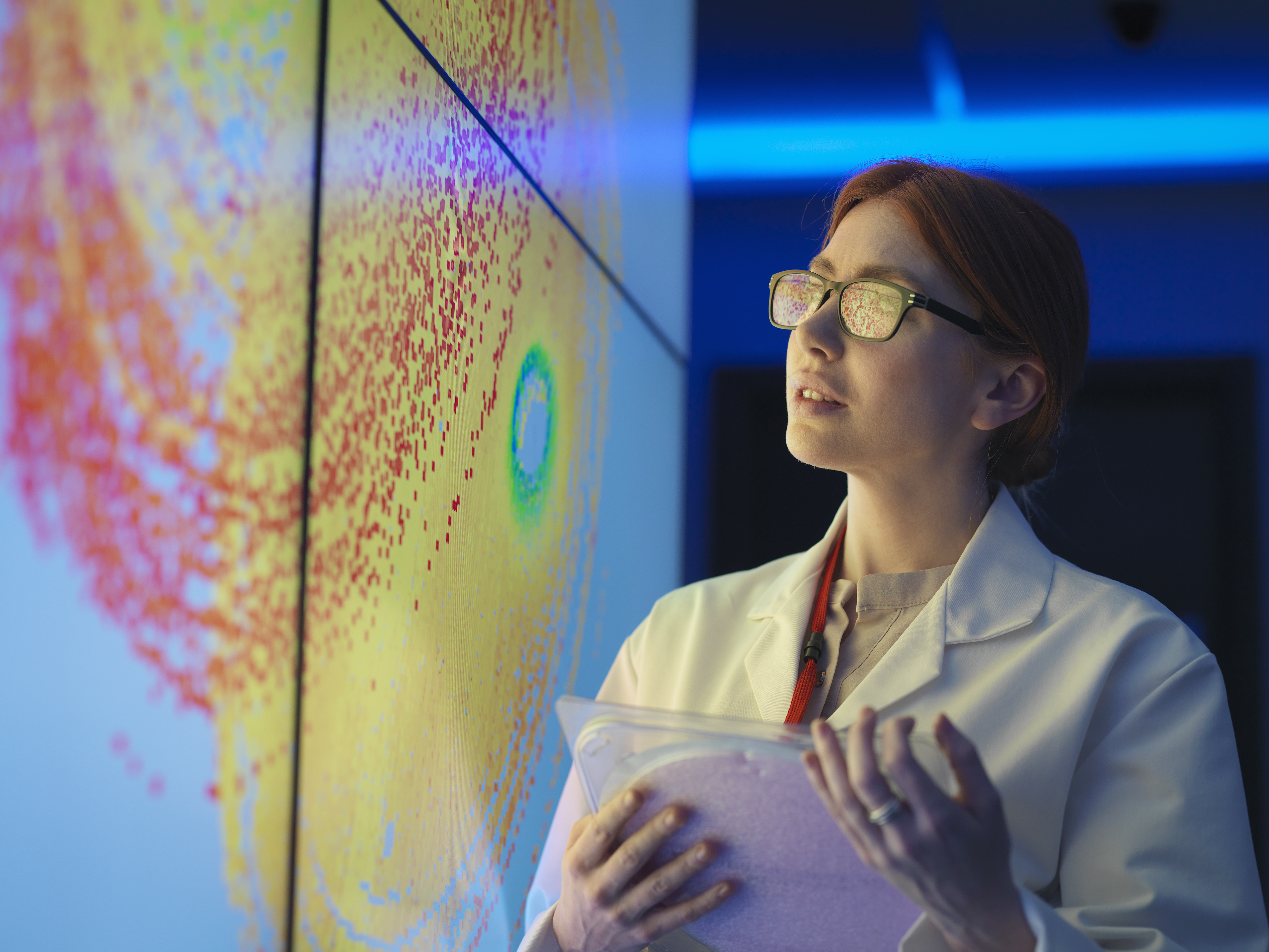 Female scientist with silicon wafer studying graphical display of wafer on screens
